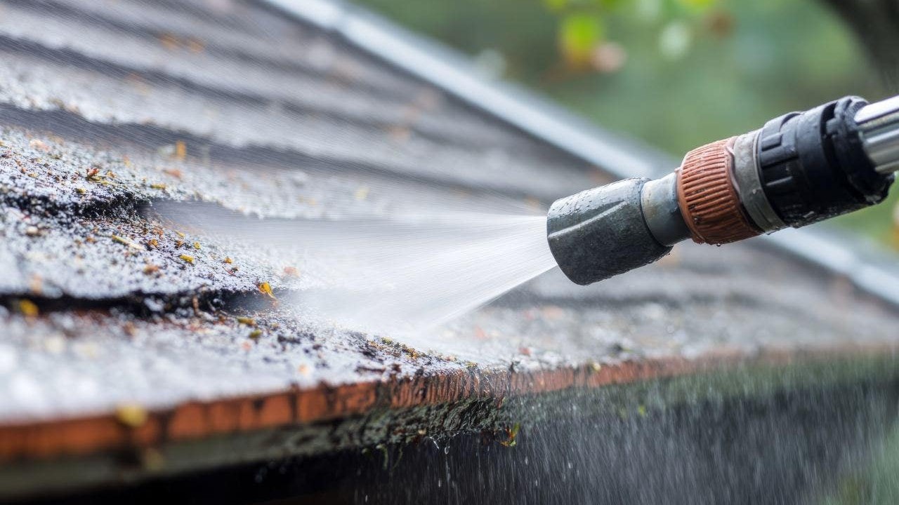 Professional soft washing a roof with visible water spray